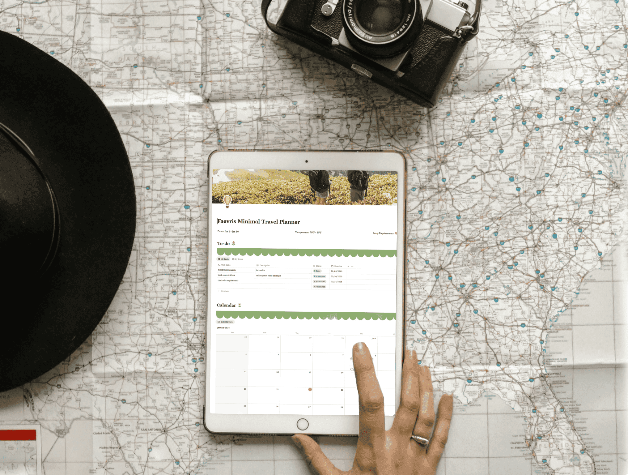 A person touching an iPad displaying a travel planner, placed on a U.S. map with a hat and camera nearby.