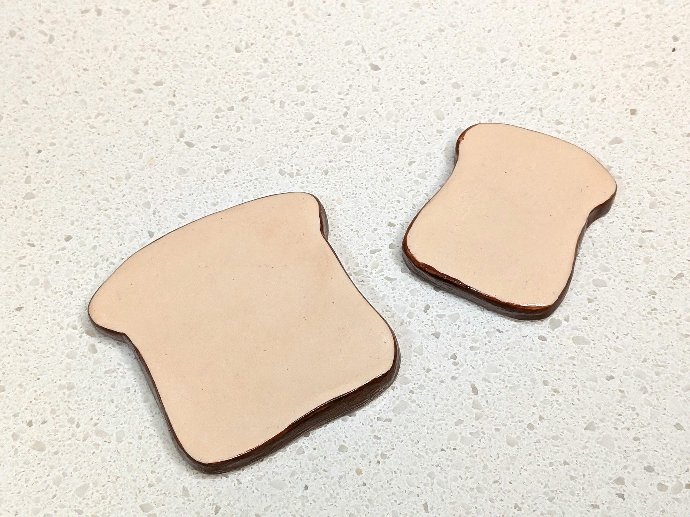 Two pieces of bread-shaped clay coasters on a speckled white countertop.