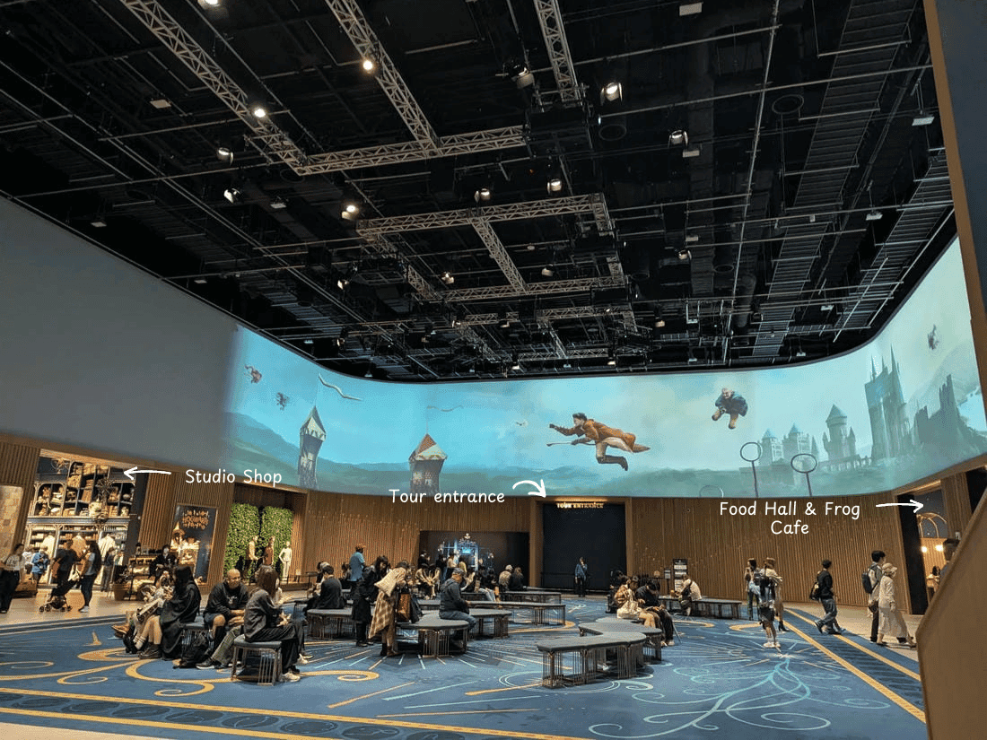 main lobby area of the harry potter studio in tokyo projector screen of quidditch match, a gift shop on the left, people sitting in the center, and food hall in the right